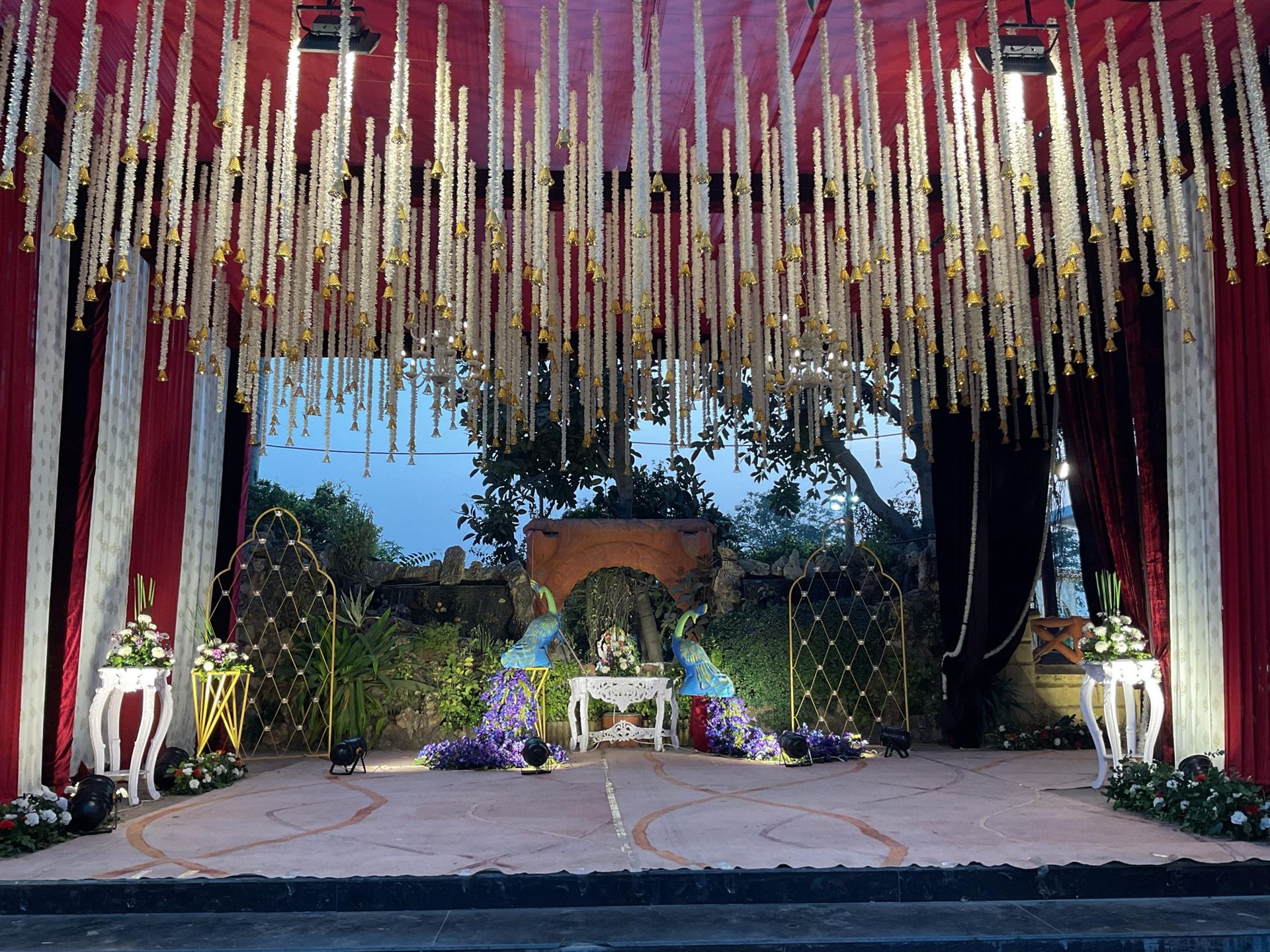 Garden wedding ceremony stage with red canopy, jasmine bells and peacock lattice decor