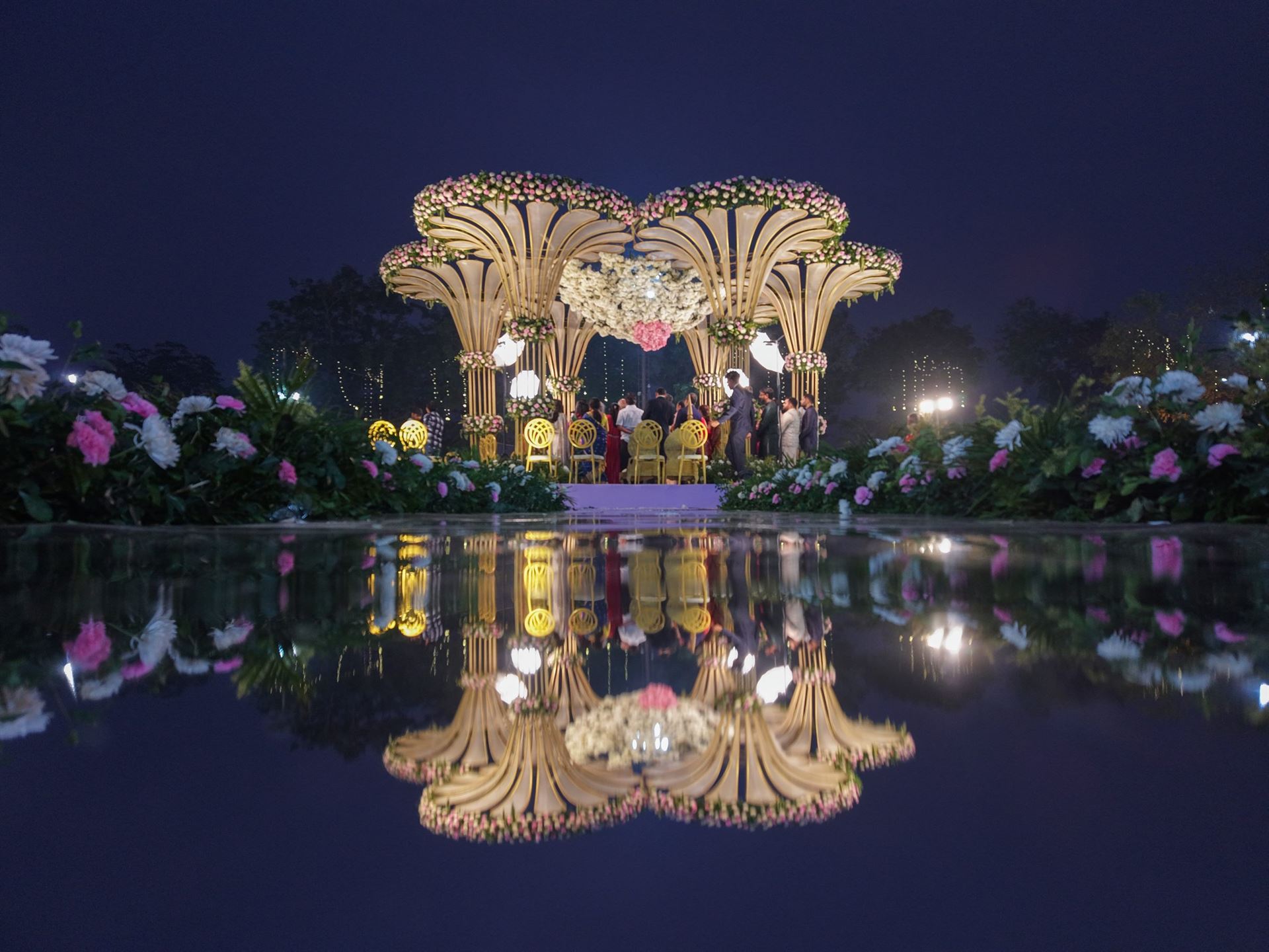 Illuminated wedding mandap beside a mirror-effect reflection pool at night