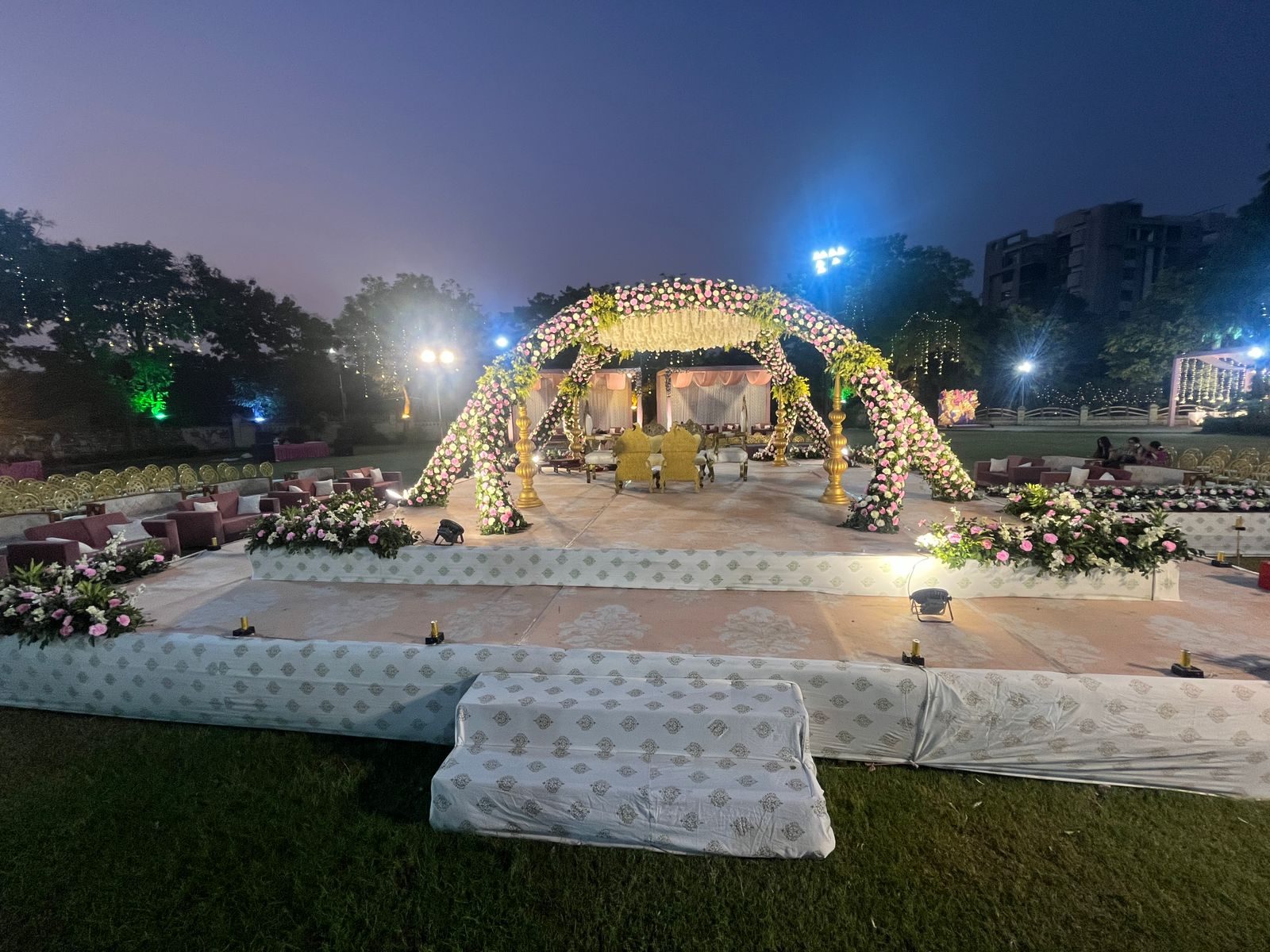Rose-clad wedding reception stage with arches on gold pillars at a twilight lawn